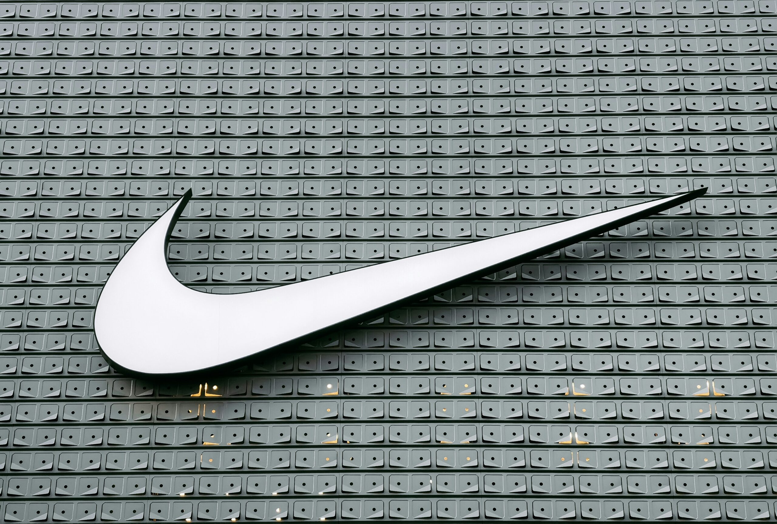Large white Nike swoosh logo displayed on a grey textured background, highlighting the brand's iconic sports identity.